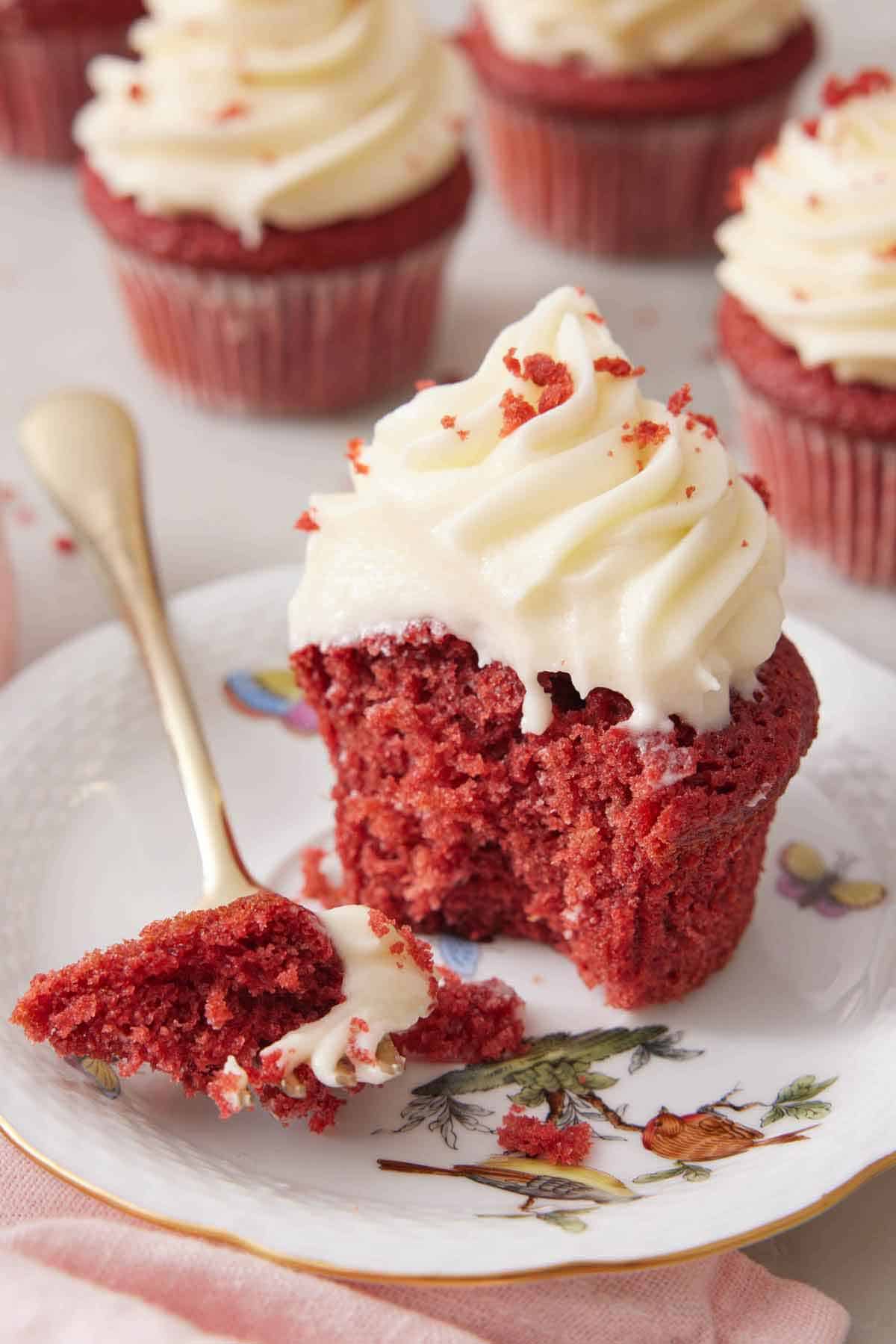 A plate with a red velvet cupcake, half eaten, with a bite on a fork.