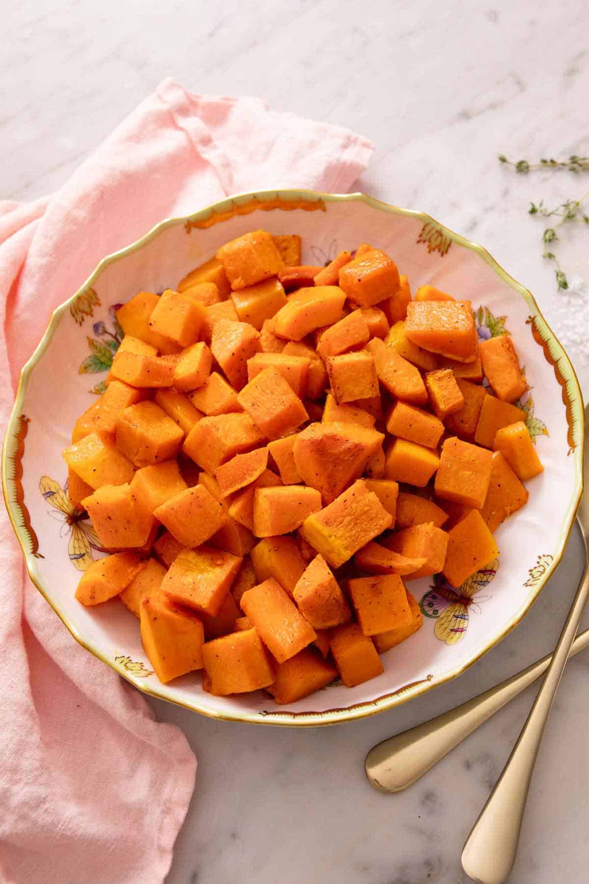 A serving plate with roasted butternut squash. Pink napkin and some forks beside it.