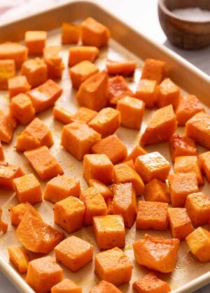 A sheet pan of roasted butternut squash. A small bowl of salt in the background.