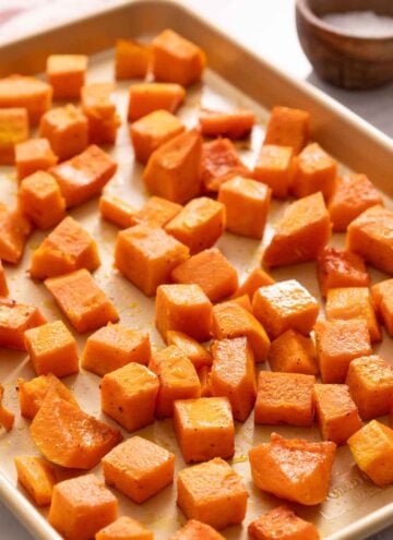 A sheet pan of roasted butternut squash. A small bowl of salt in the background.