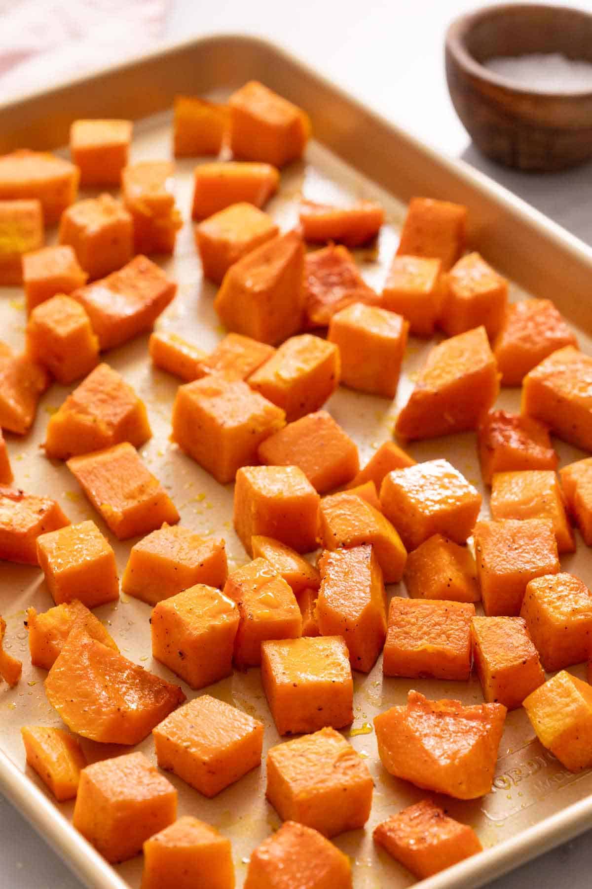 A sheet pan of roasted butternut squash. A small bowl of salt in the background.