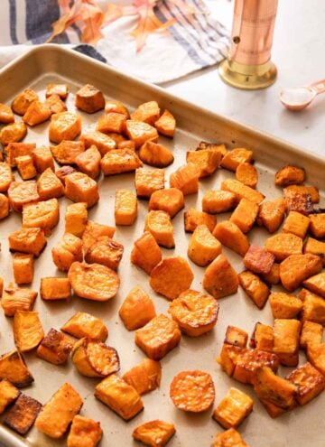 A sheet pan of roasted sweet potatoes with a pepper grinder in the back and some salt.
