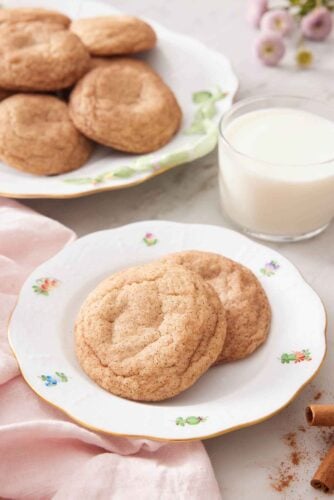 A plate with two snickerdoodle cookies with a glass of milk and additional cookies in the background.