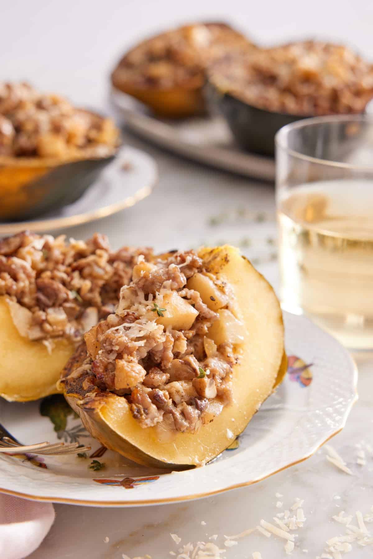 A plate with a stuffed acorn squash cut in half with a glass of wine and additional squash in the background.