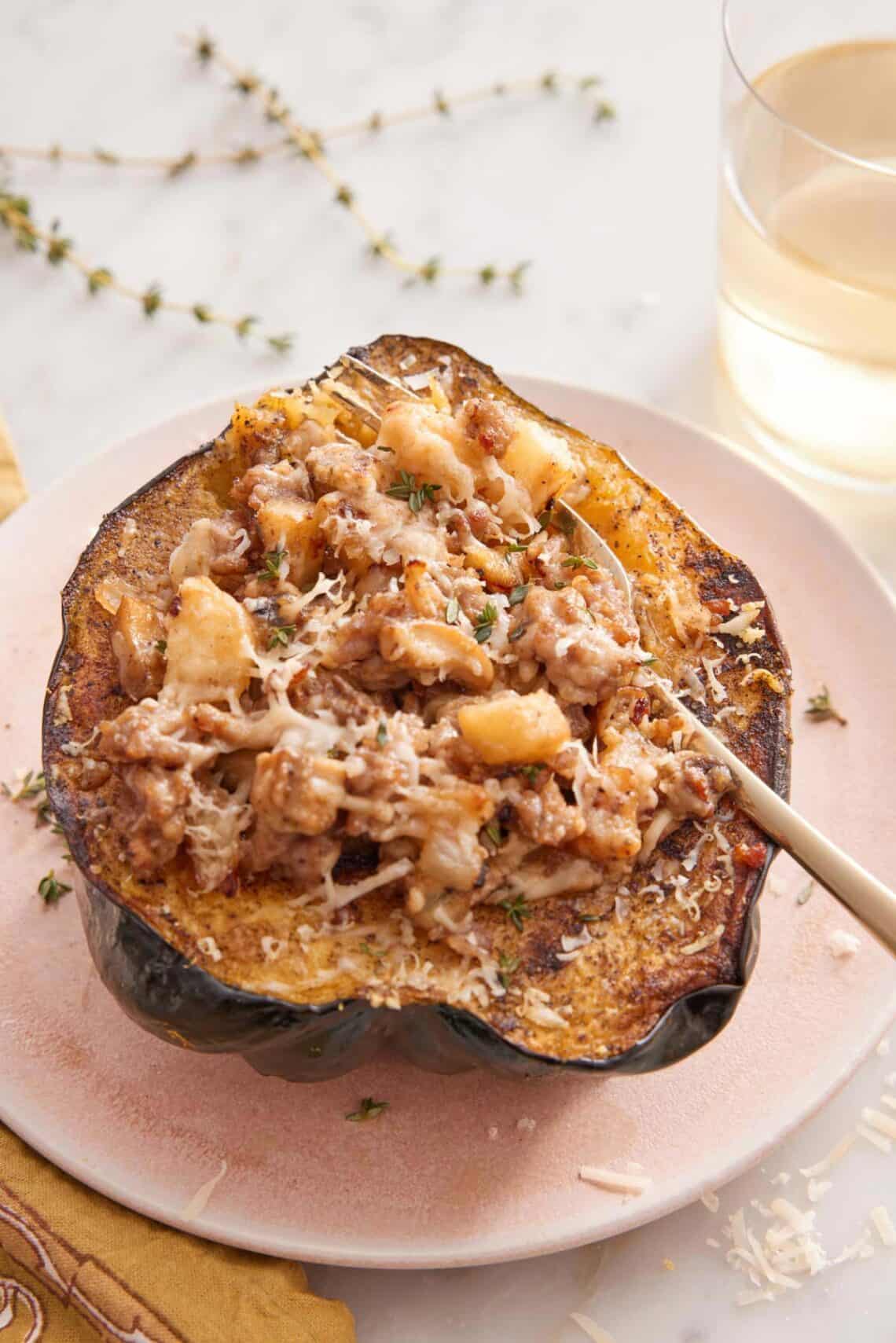 A plate with a serving of stuffed acorn squash with a fork inside. Glass of wine and thyme in the background.
