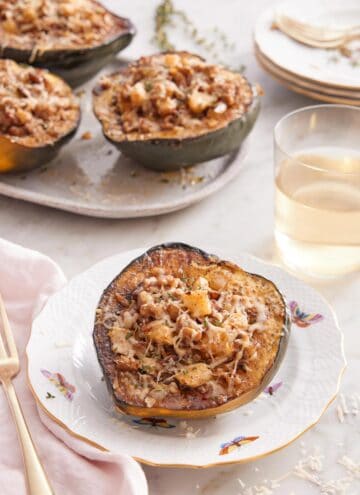 A plate with a stuffed acorn squash with a glass of wine and platter of more squash in the background.