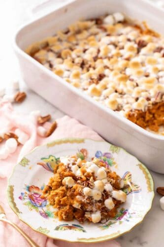 A plate with serving of sweet potato casserole with a baking dish of it in the background.