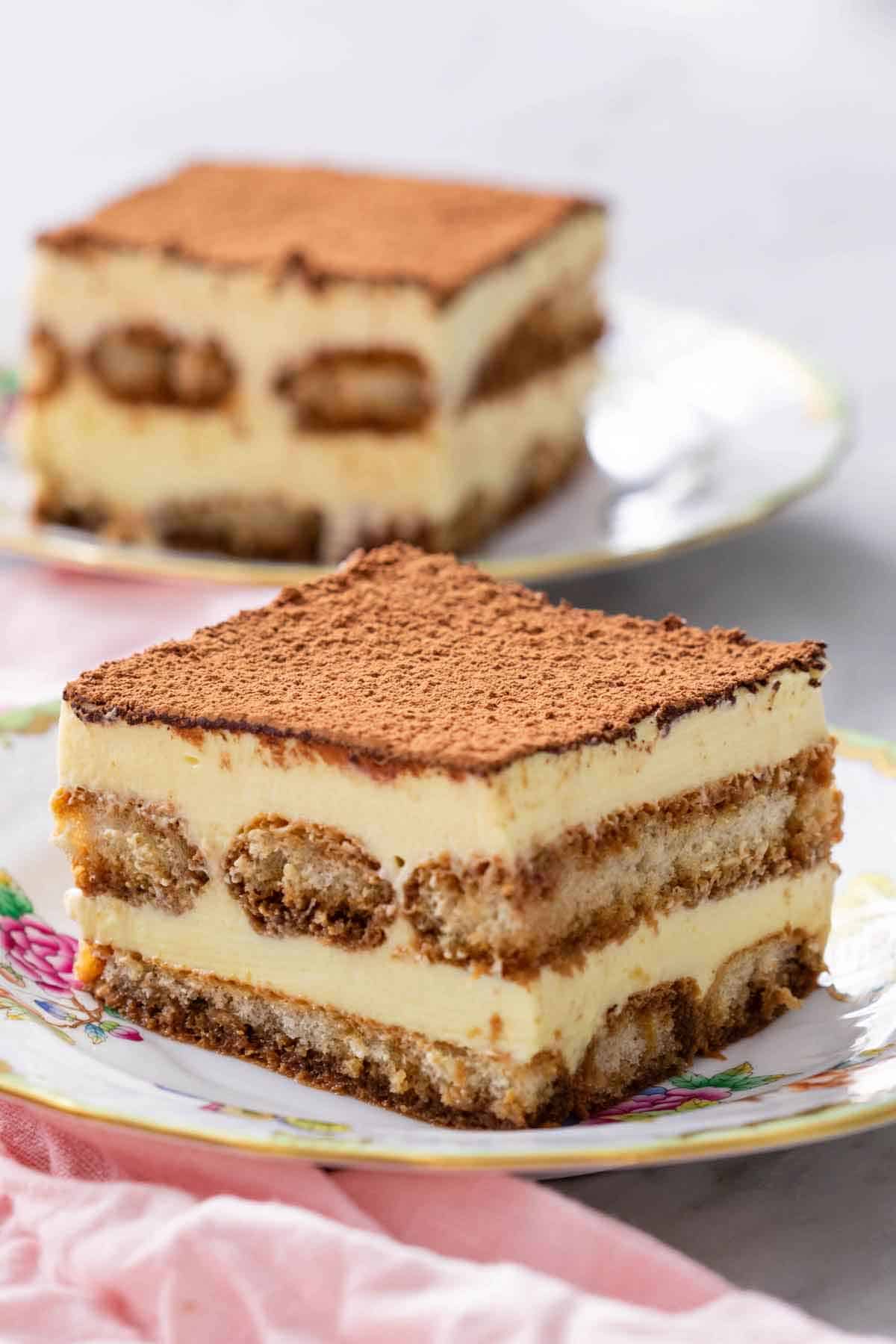 A profile view showing the layers of tiramisu on a plate. A second piece of tiramisu in the background.