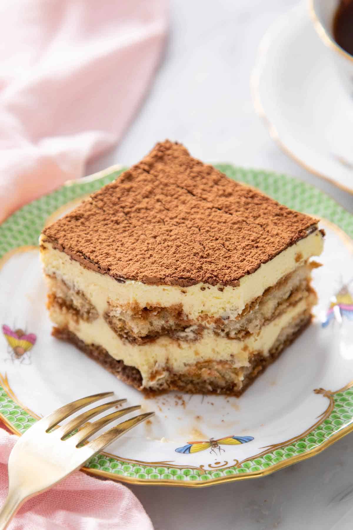 A slice of tiramisu on a plate with a bite taken out and a fork beside it.