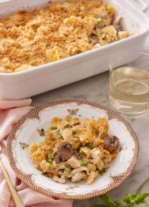 A plate with a serving of turkey casserole with a glass of wine and baking dish behind it.