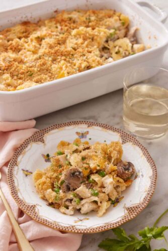A plate with a serving of turkey casserole with a glass of wine and baking dish behind it.
