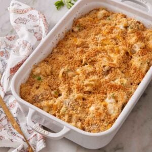 A white baking dish with turkey casserole with a serving spoon, napkin, and plate to the side.