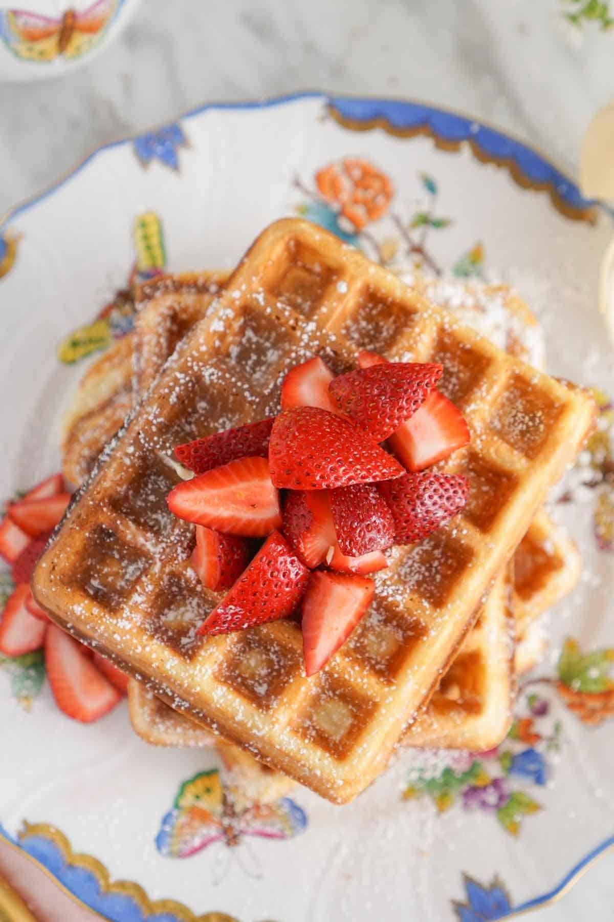 Overhead view of strawberries on top of a stack of waffles dusted with powdered sugar.