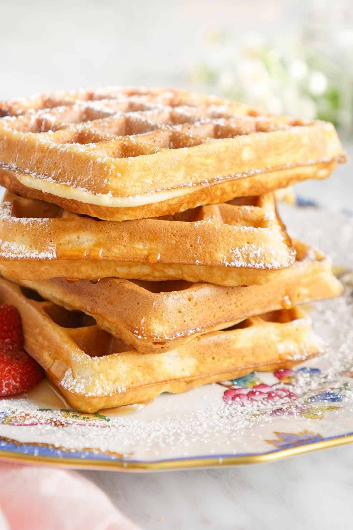 A profile view of a stack of waffles with powdered sugar dusted on top.