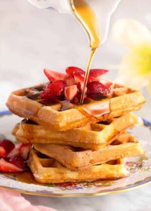 A stack of waffles and strawberries with syrup poured over top.