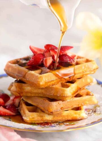 A stack of waffles and strawberries with syrup poured over top.