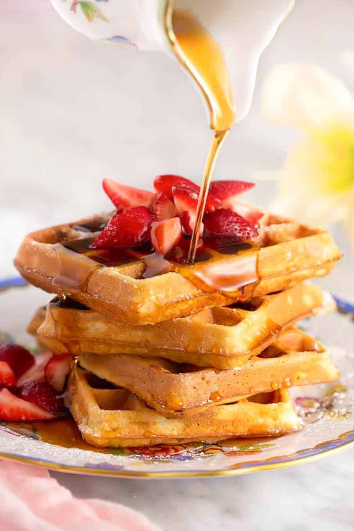 A stack of waffles and strawberries with syrup poured over top.