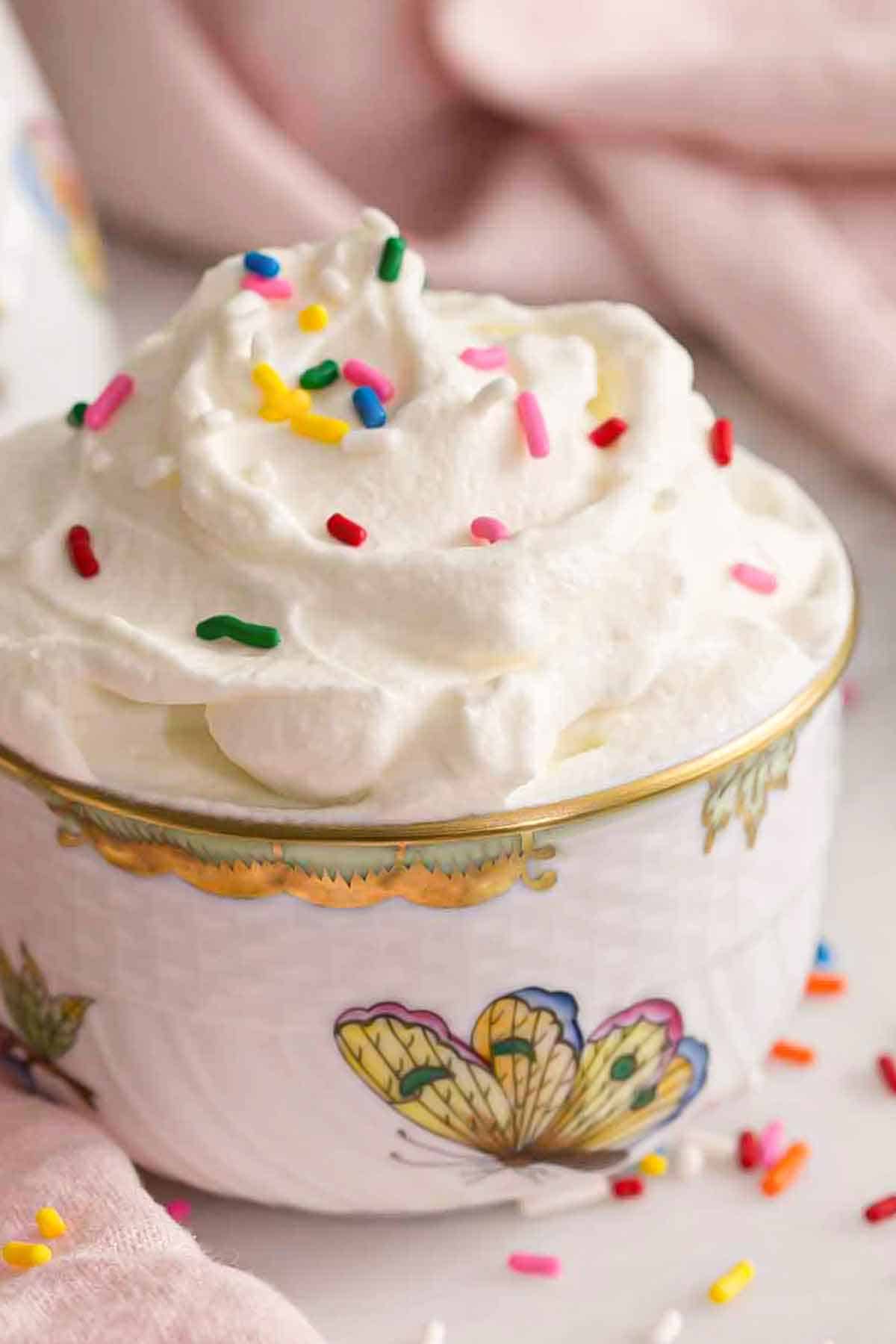 A profile view of a bowl of whipped cream topped with rainbow sprinkles.