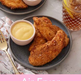 Pinterest graphic of a plate of three air fryer chicken tenders with a small bowl of mustard. More tenders and a drink in the background.