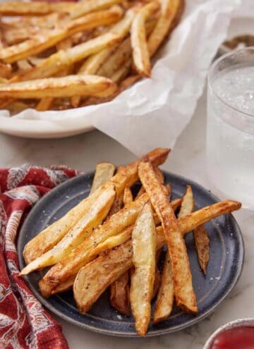 A plate with air fryer french fries with a drink and more fries in the background.
