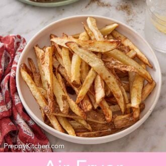 Pinterest graphic of a white plate containing air fryer french fries with more fries in the background with a drink and pepper in a small bowl.