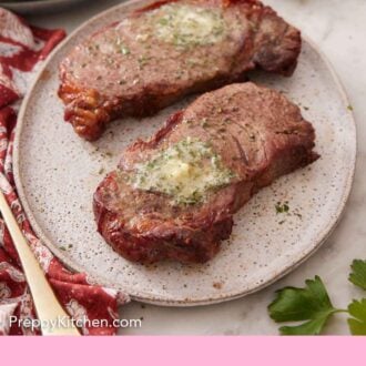 Pinterest graphic of a plate with two pieces of air fryer steak topped with melted herb butter. A stack of plates and forks in the background.