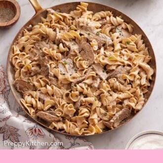 Pinterest graphic of a skillet of beef stroganoff with some torn bread and a stack of plates with forks off to the side.
