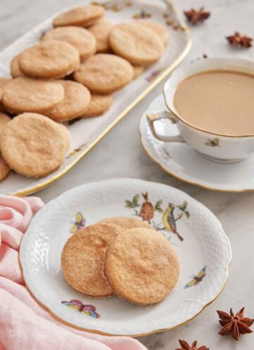 A plate with three biscochitos with a drink in the background with a platter of more cookies.