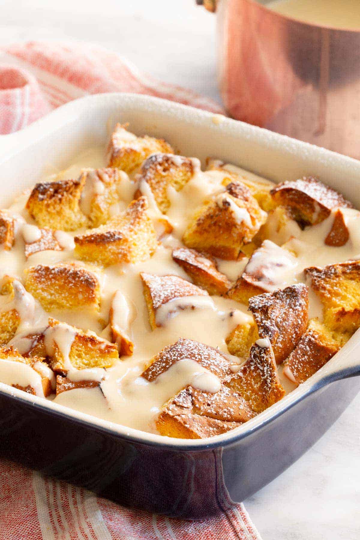 A baking dish of bread pudding with vanilla sauce on top.