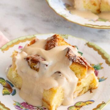 A plate with a serving of bread pudding with a second one in the background, slightly out of frame.