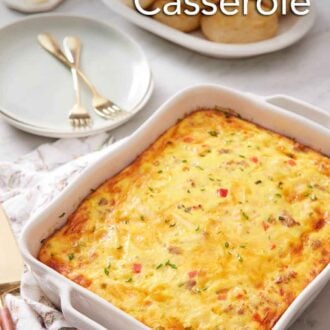 Pinterest graphic of breakfast casserole in a baking dish with a plate of rolls and stack of plates with forks in the background.