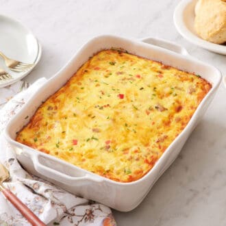A baking dish of breakfast casserole with bread and butter off to the side along with plates and forks.
