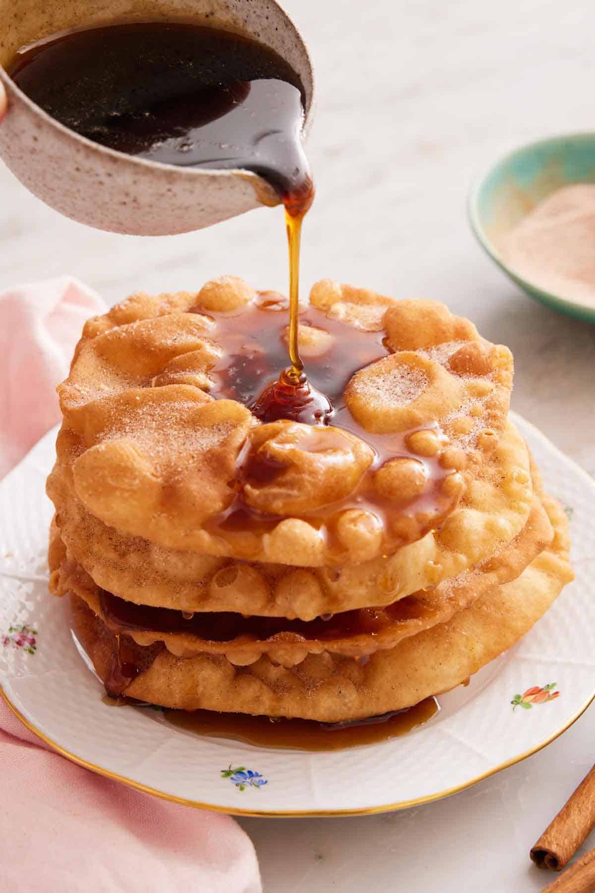 A plate with a stack of bunuelos with piloncillo syrup poured on top.