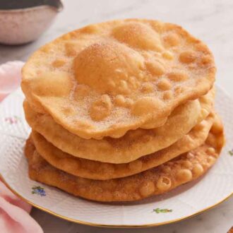 A plate with a stack of bunuelos topped with cinnamon sugar.
