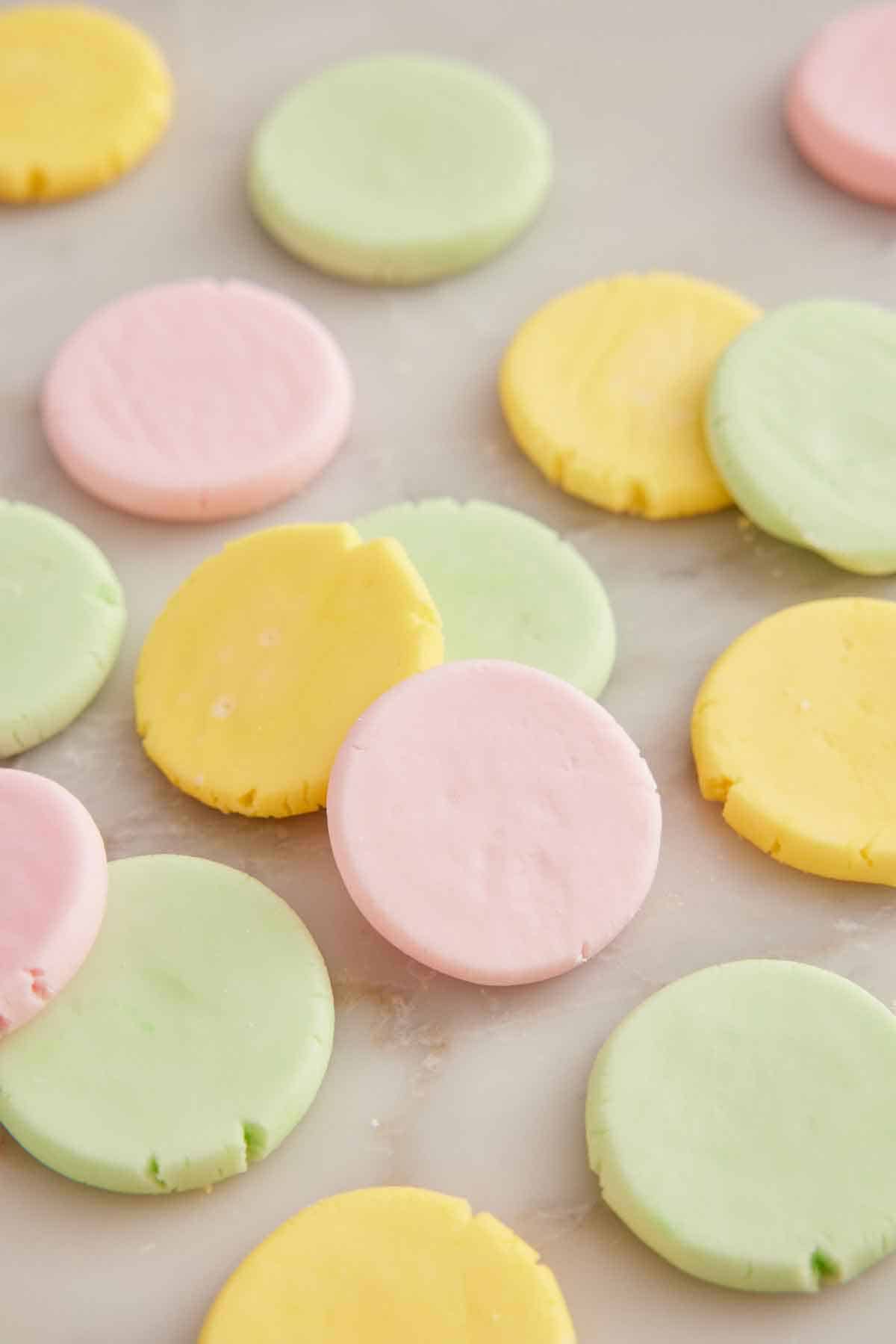 Multiple multi-colored butter mints flattened into circles on a marble surface.