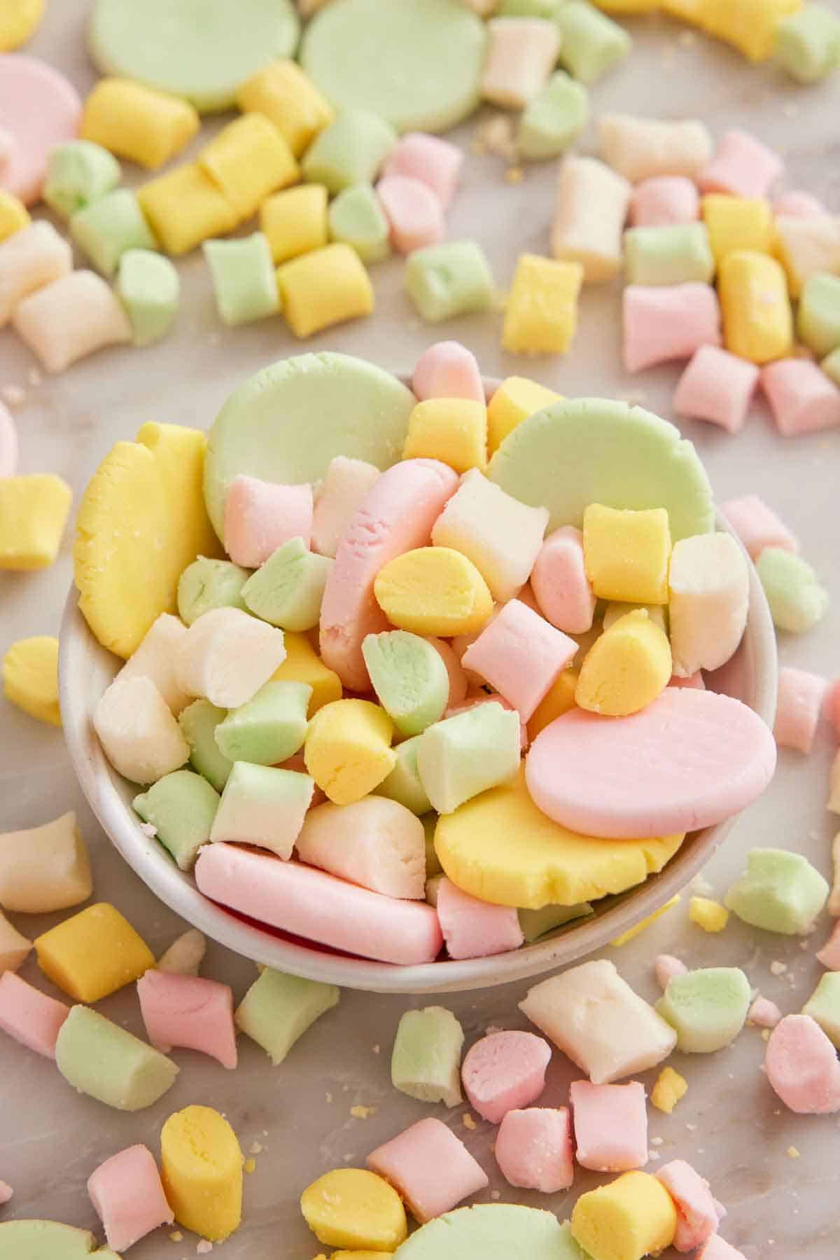 A bowl of butter mints, some flattened into coin shapes with more surrounding the bowl.
