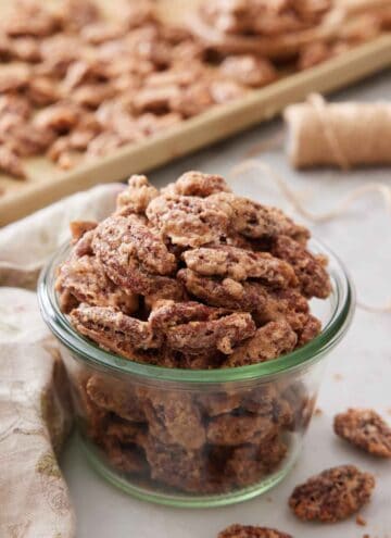 A jar of candied pecans with some on a sheet pan in the background.