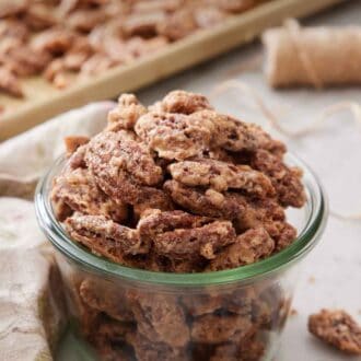 Pinterest graphic of a jar of candied pecans with some on a sheet pan in the background.