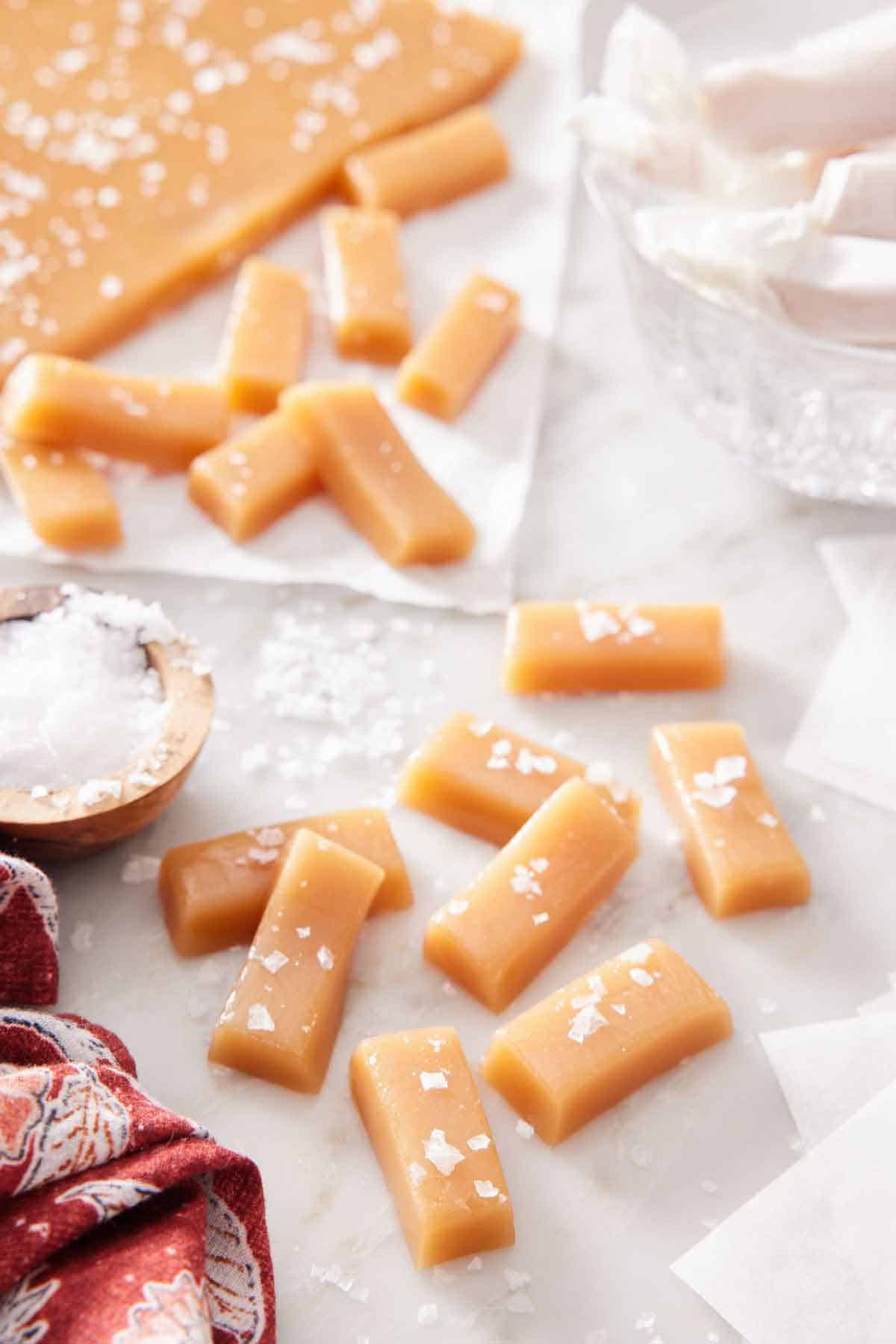 Multiple pieces of caramels with additional in the background, topped with sea salt.