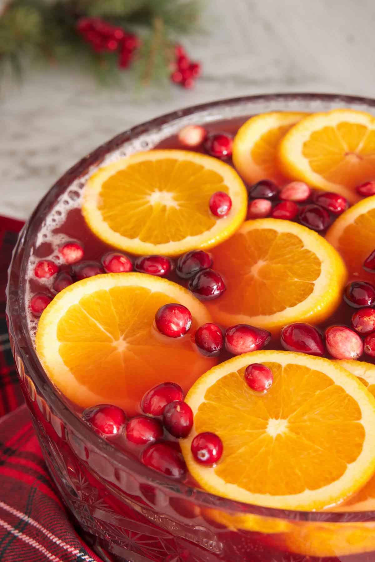 A large bowl of Christmas punch topped with freshly sliced oranges and cranberries.