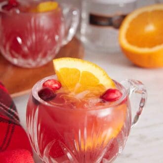 Pinterest graphic of a glass of Christmas punch with orange and cranberries with more fruit scattered around.