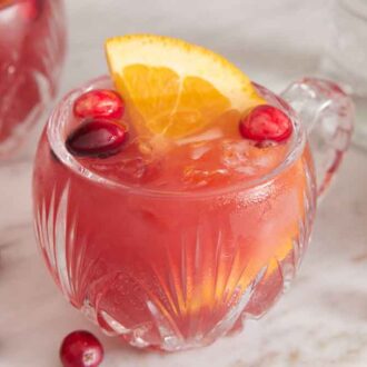 A glass of Christmas punch with cranberries scattered around.