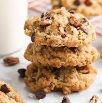 A stack of three cowboy cookies with additional ingredients scattered around.