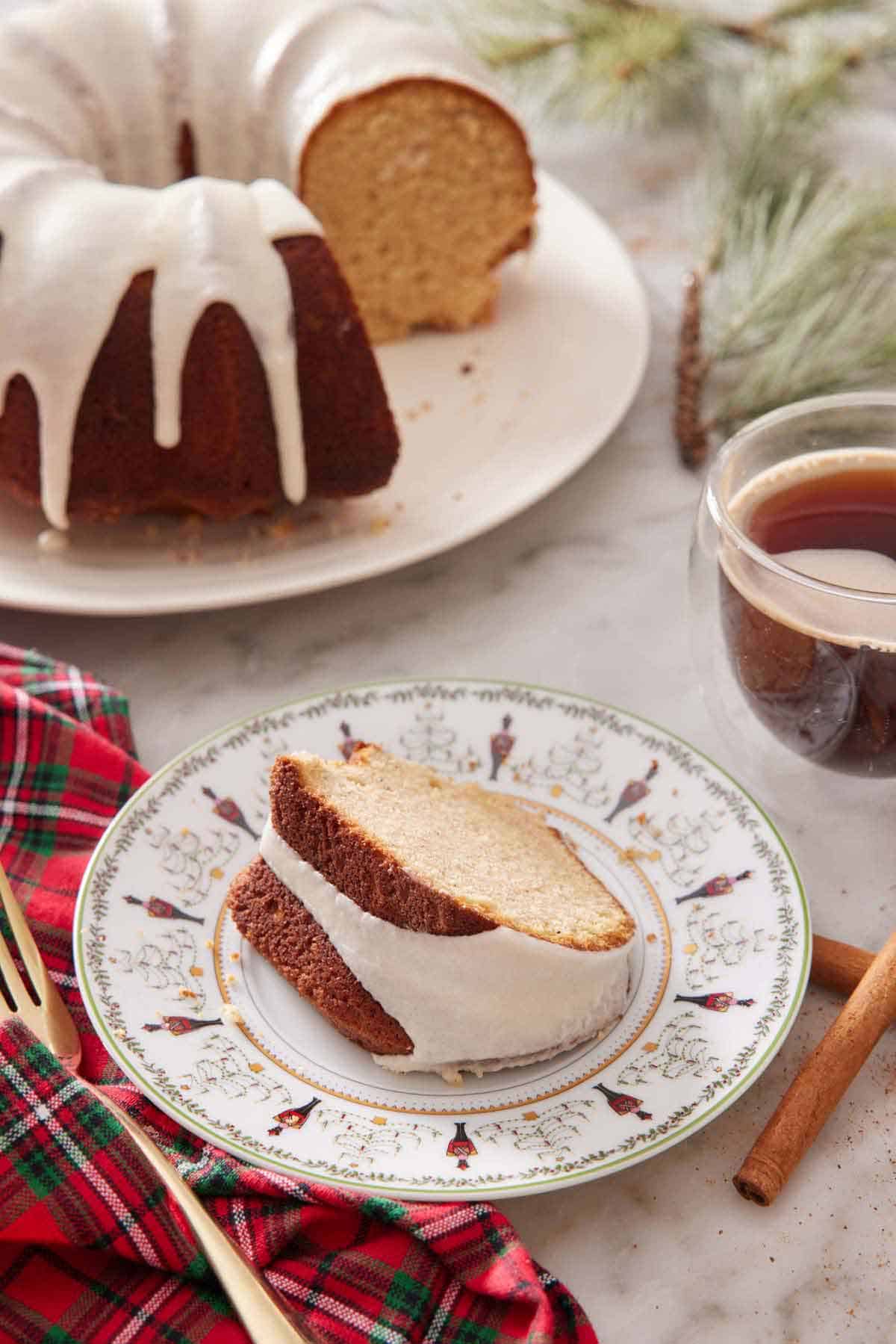 A plate with a slice of eggnog cake with the rest of the cake in the background.