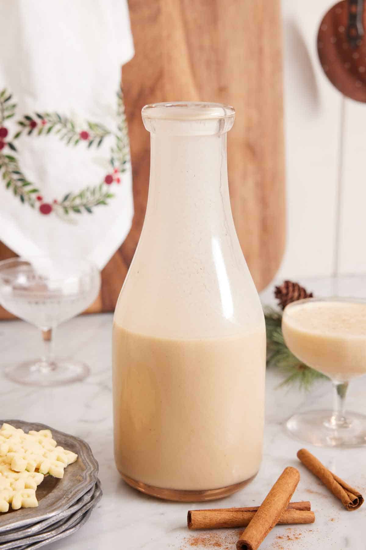 A bottle of eggnog with a full glass off to the side and empty glass in the back.