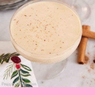 Pinterest graphic of a slightly overhead view of a glass of eggnog with cinnamon sprinkled on top.
