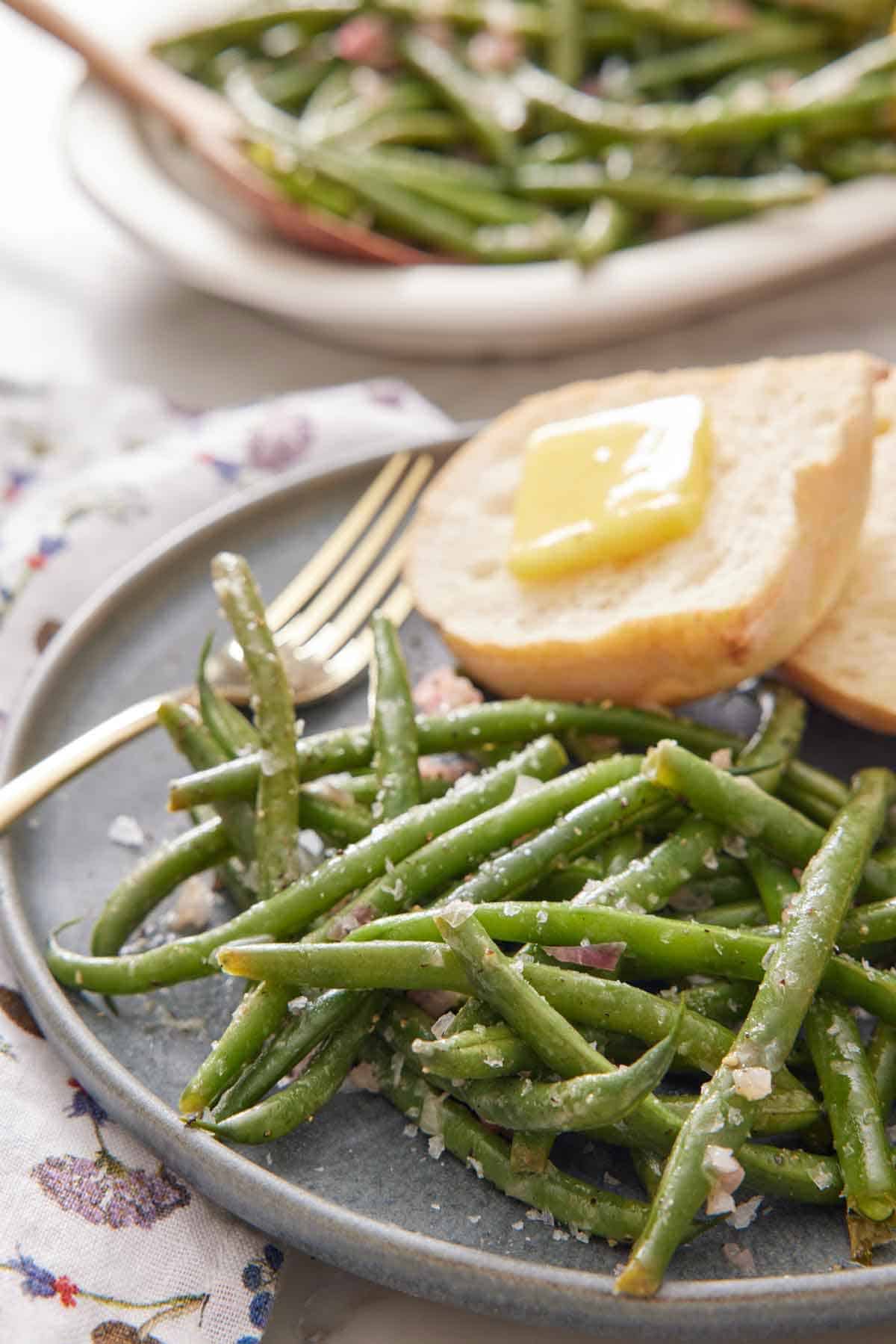A close up view of French green beans on a plate with a fork and bread with some butter on it.