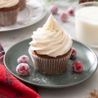A plate with a gingerbread cupcake with some sugared cranberries beside it. A glass of milk behind it.