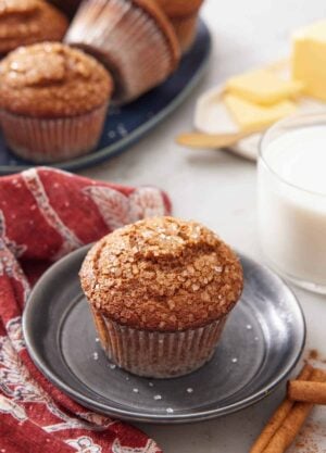 A plate with a gingerbread muffins with a glass of milk and platter of more muffins in the background.