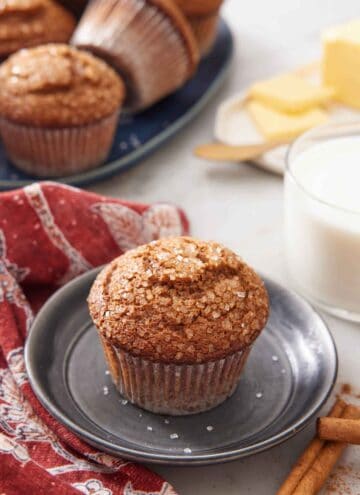 A plate with a gingerbread muffins with a glass of milk and platter of more muffins in the background.
